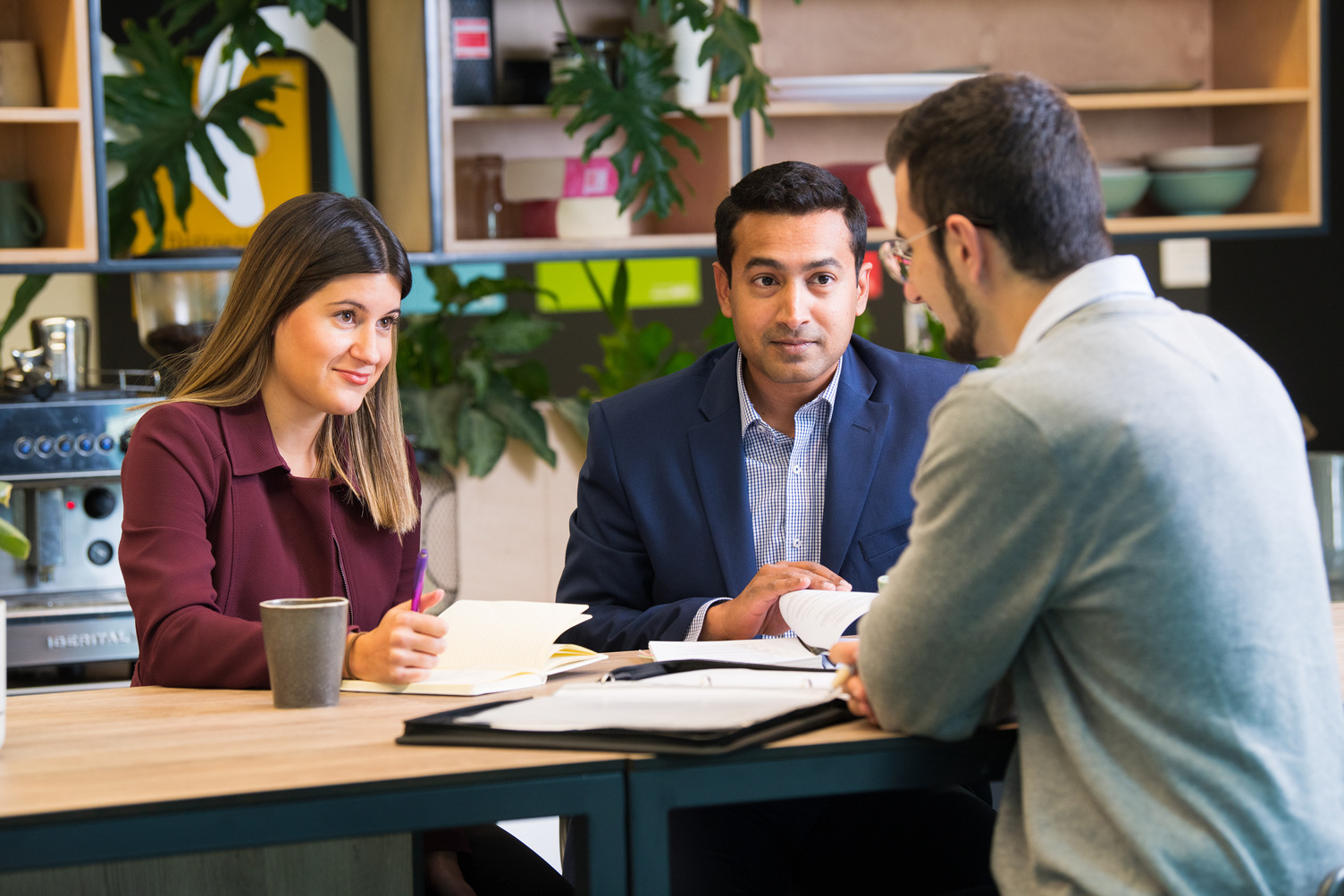 A group of three people sitting at a desk together with papers between them