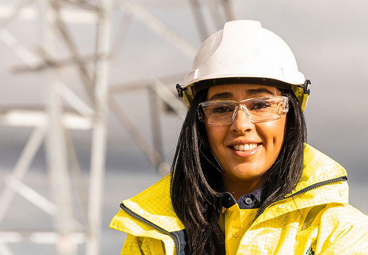 A smiling woman in hi-vis clothing near a large powerline